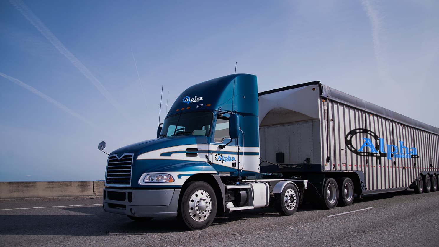 An Alpha Trans Mack tractor in company livery hauling a curtain-side trailer